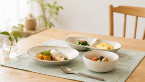 明るい食卓に、縁のある浅皿と小鉢、仕切り皿、スプーンを並べた様子